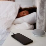 Frau im Bett beim Schlafen mit Handy und Smart Speaker